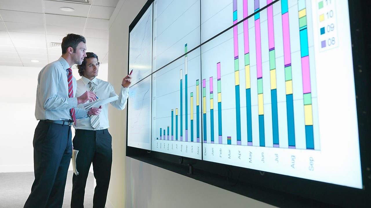 Business men analyse reports displayed on a large digital screen