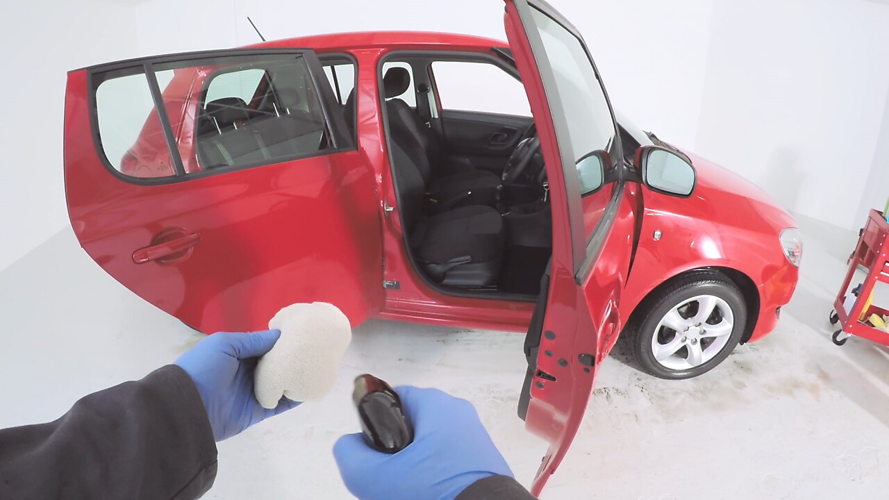 hands with a cleaning spray and mop preparing to clean inside a red car