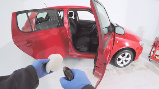 hands with a cleaning spray and mop preparing to clean inside a red car