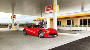 Një Ferrari i kuq i parkuar në një ndërtesë të Shell me një burrë të mbështetur në një pompë benzine