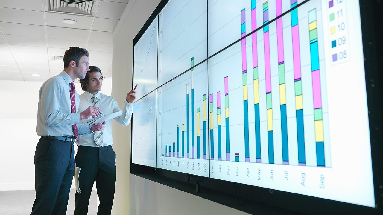 Business men analyse reports displayed on a large digital screen
